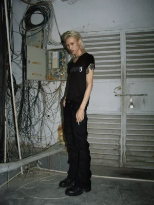 Black slim flare streetwear trousers paired with a minimalist black short-sleeve tee in an industrial interior