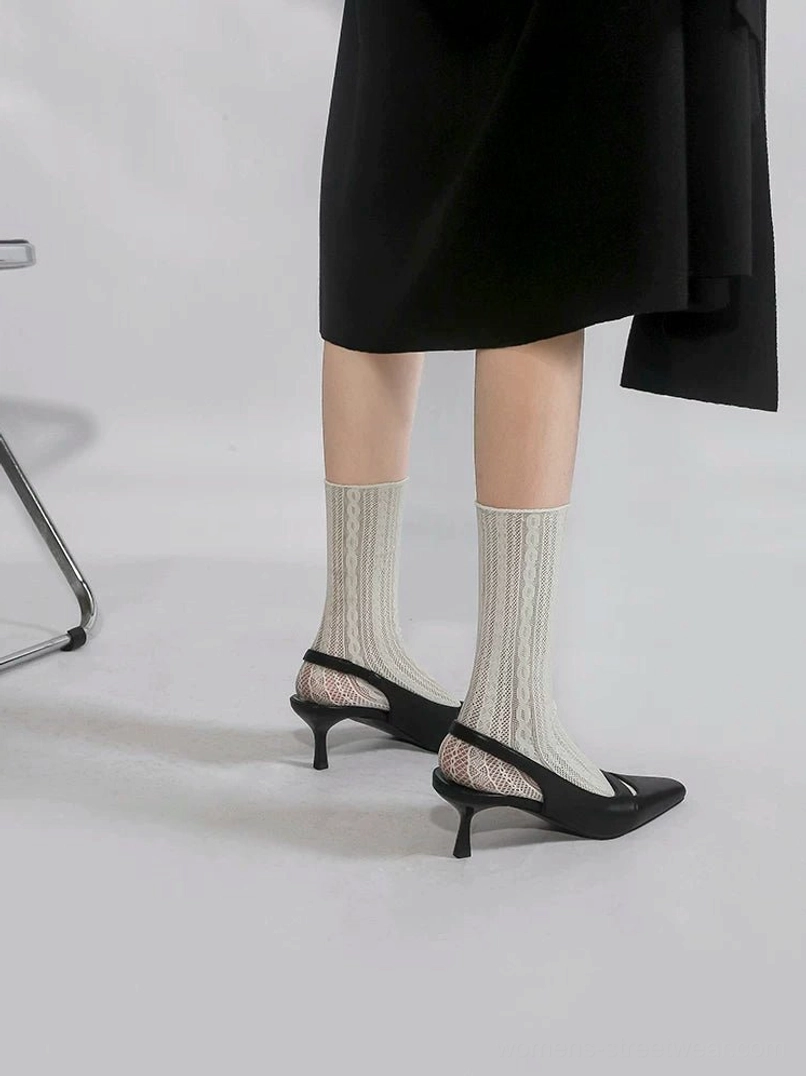Rear low-angle view of black slingback kitten heels showing the exposed heel, slim strap, narrow 5 cm heel, tailored black skirt, and cream cable-knit socks