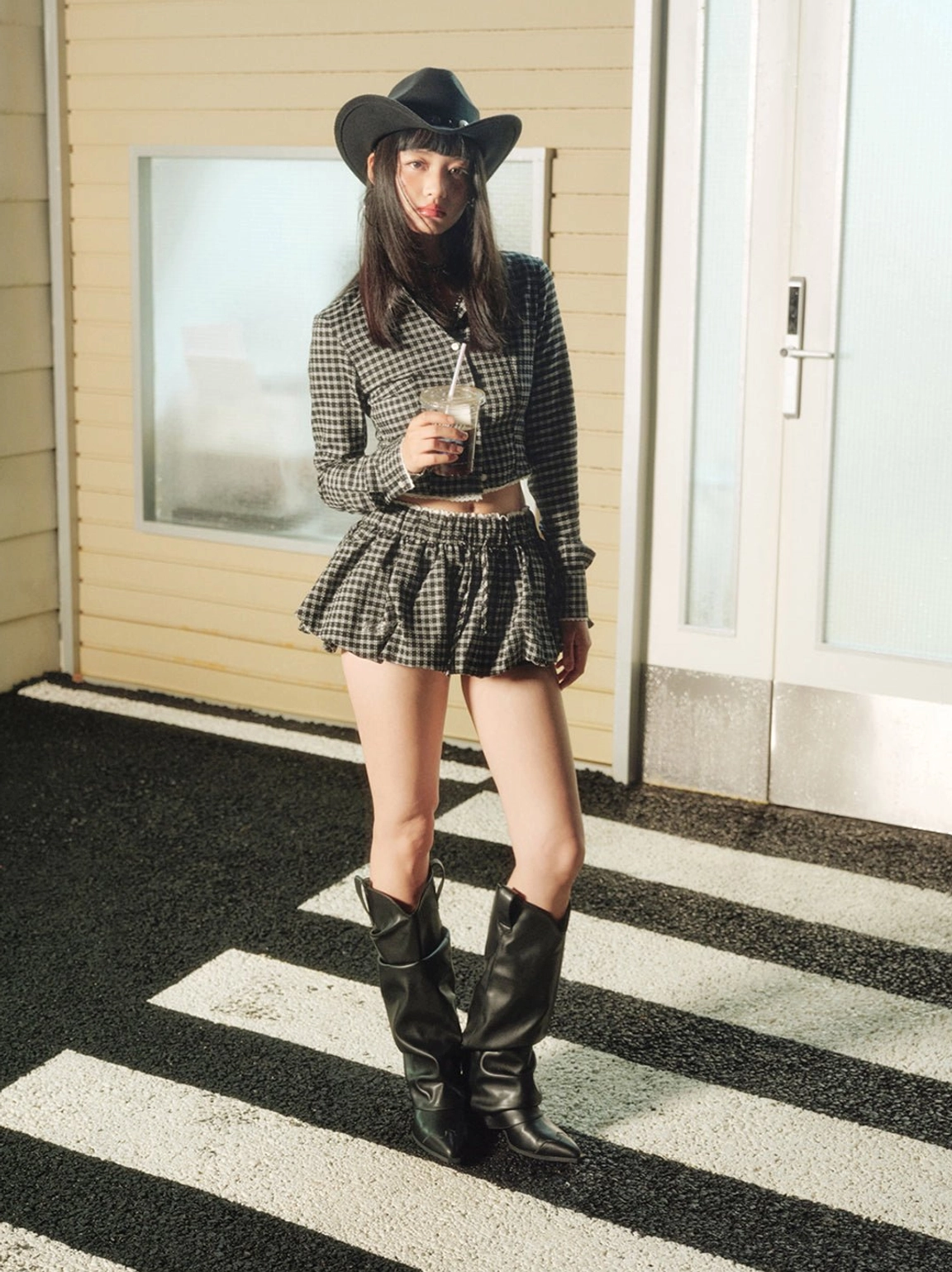 Front view of black slouched knee-high cowboy boots with pointed toes worn with a cropped blazer and mini skirt