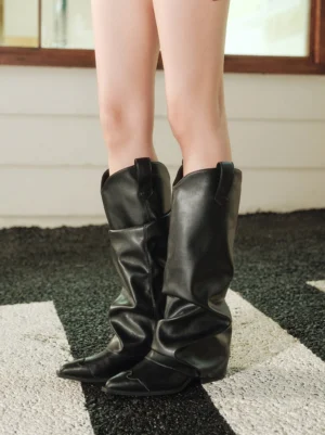 Close-up view of black slouched knee-high Western boots on female legs showing the oversized relaxed shaft and pointed toe