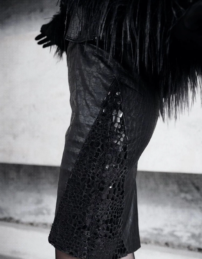 Low angle side detail of black coated leather-look pencil skirt with vertical semi-sheer snakeskin mesh inserts