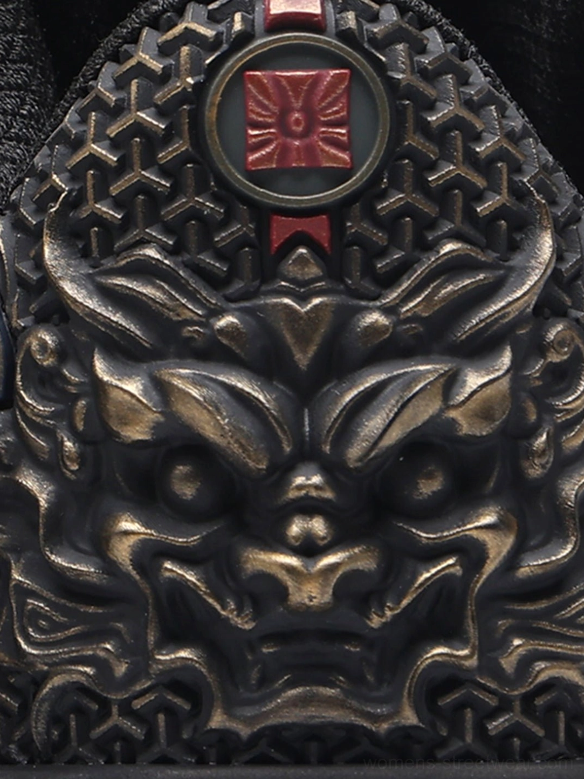 Close-up of black sneaker heel featuring a fierce bronze dragon carving, red emblem, and geometric perforated texture