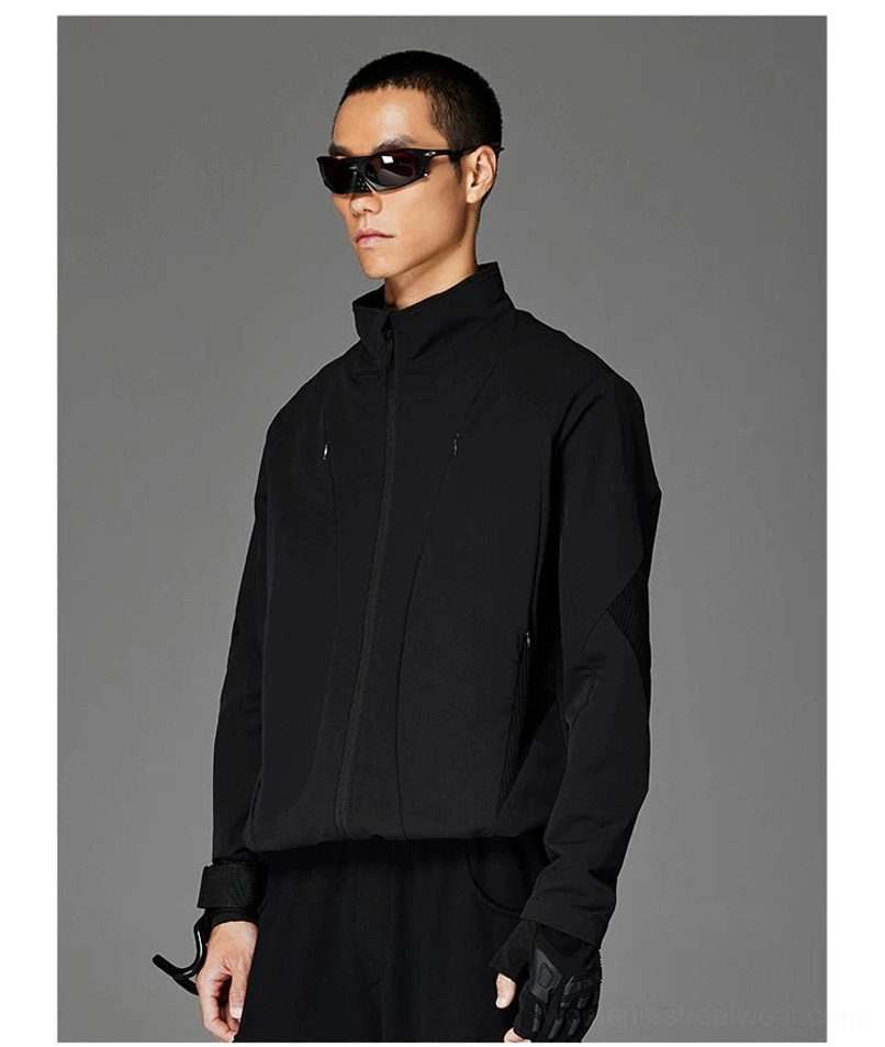 Male model wearing a black stand-collar softshell techwear jacket with sport sunglasses, tactical fingerless gloves, and matching black streetwear bottoms