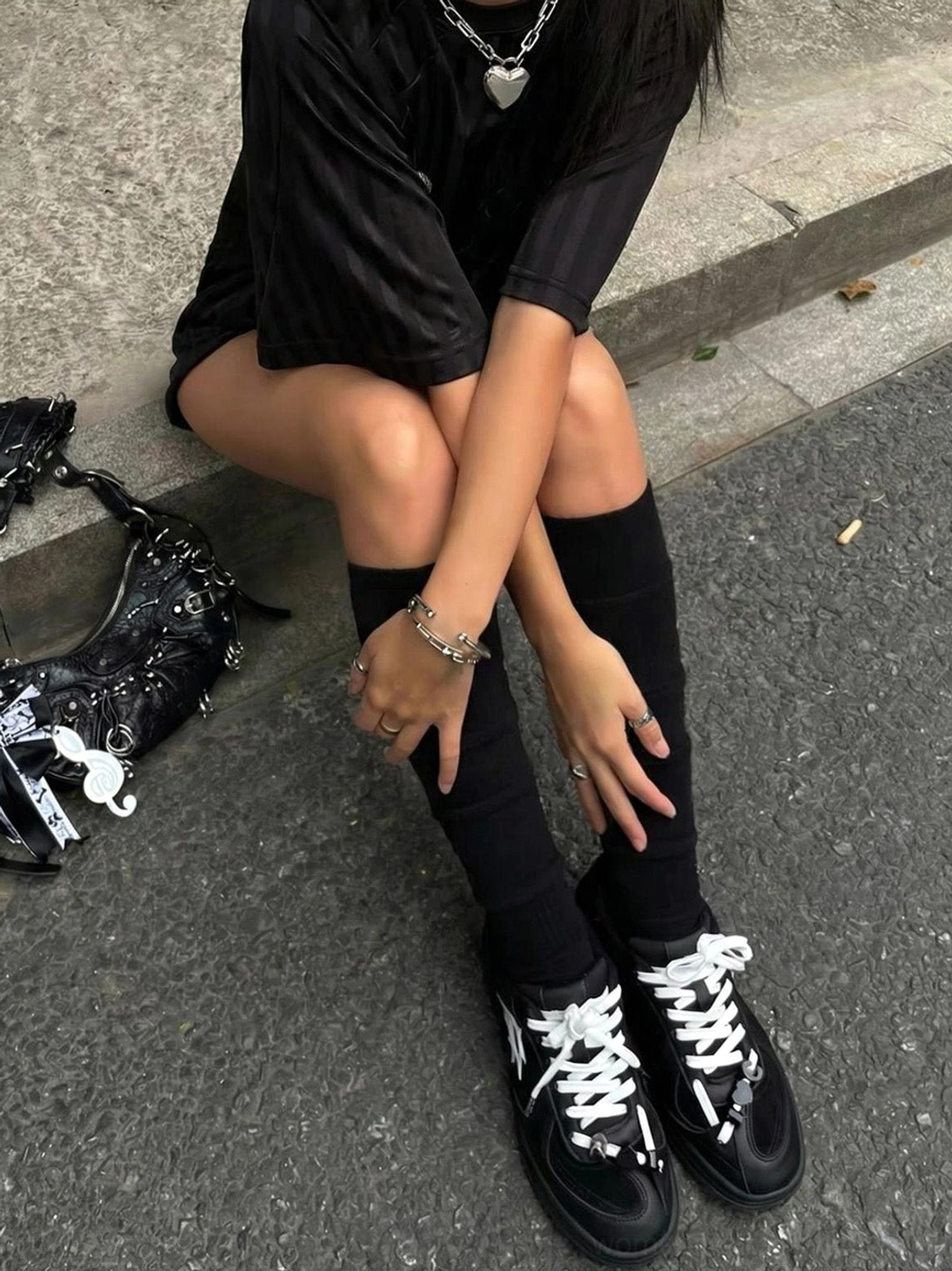 Black solar star applique court sneaker worn with long black socks and a black streetwear outfit on an urban pavement