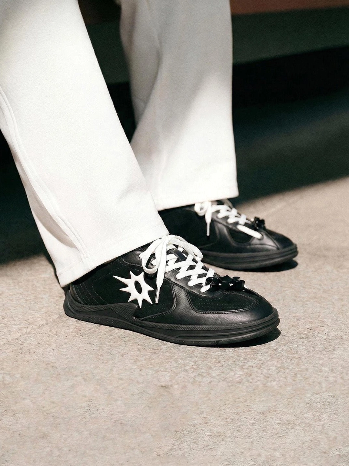 Black leather solar star applique court sneakers paired with white tailored trousers and decorative lace charms