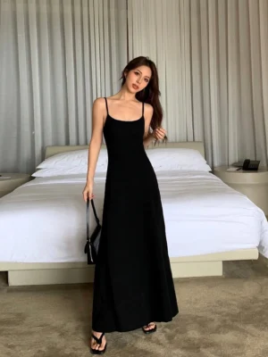 Black spaghetti strap maxi slip dress shown from the front in a minimalist bedroom with a sleek floor length silhouette
