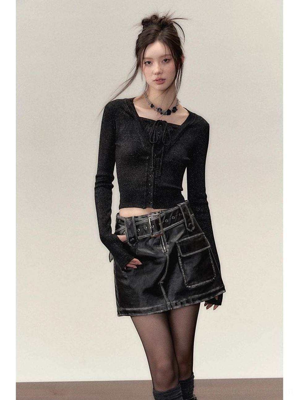 Model wearing a black sparkly faux two-piece cropped knit top with fitted long sleeves, cargo leather mini skirt, sheer stockings and biker boots in an edgy streetwear outfit