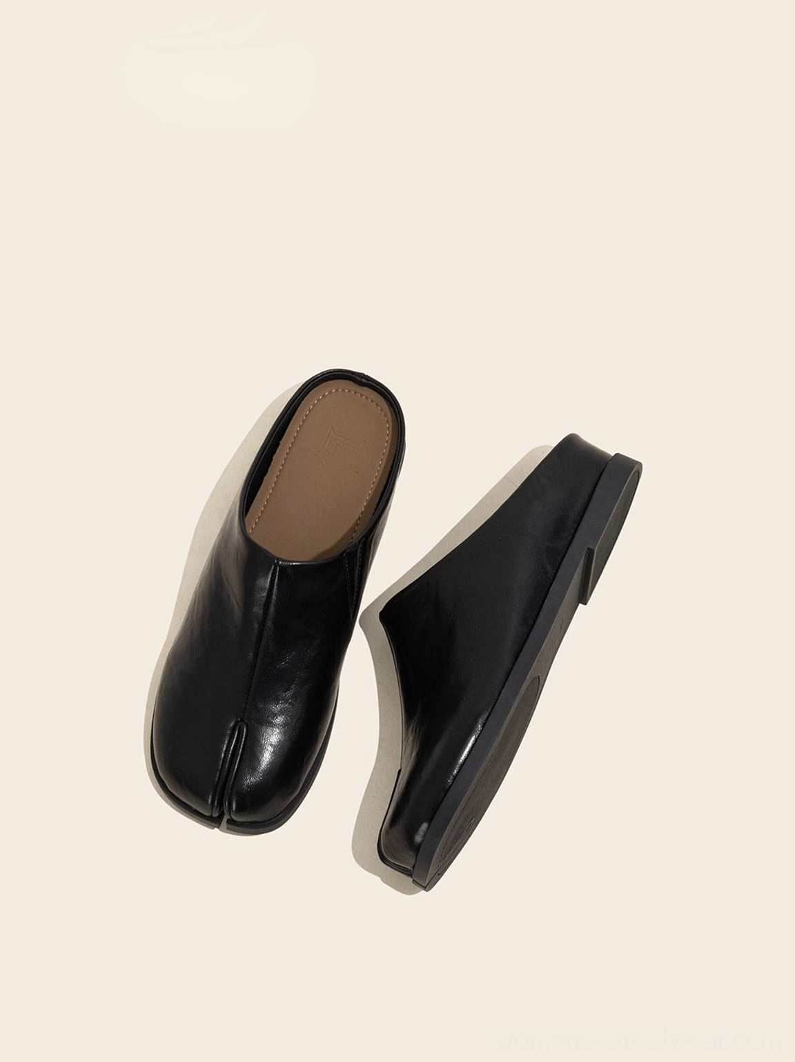 Black split-toe backless flat mules displayed at an angle to show the open heel and flat sole