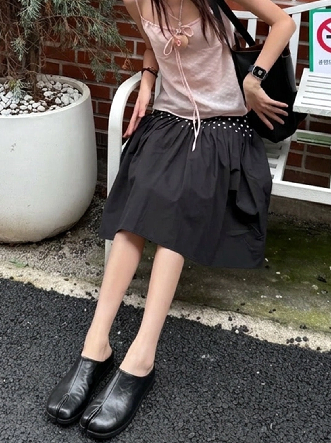 Black leather split-toe flat mules styled with a pink camisole and black ruffled skirt for casual streetwear
