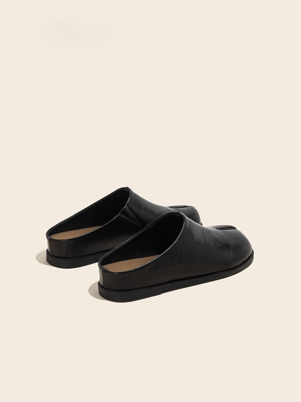 Low-angle view of black split-toe leather flat mules showing the thick flat sole and slip-on structure