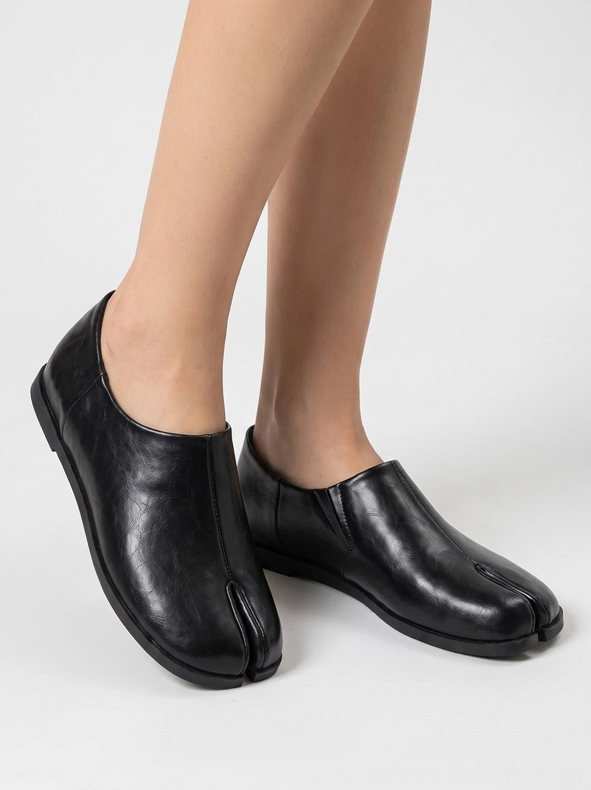 Close-up front view of black split-toe leather loafers showing natural texture, center seam, slip-on collar, and flat sole