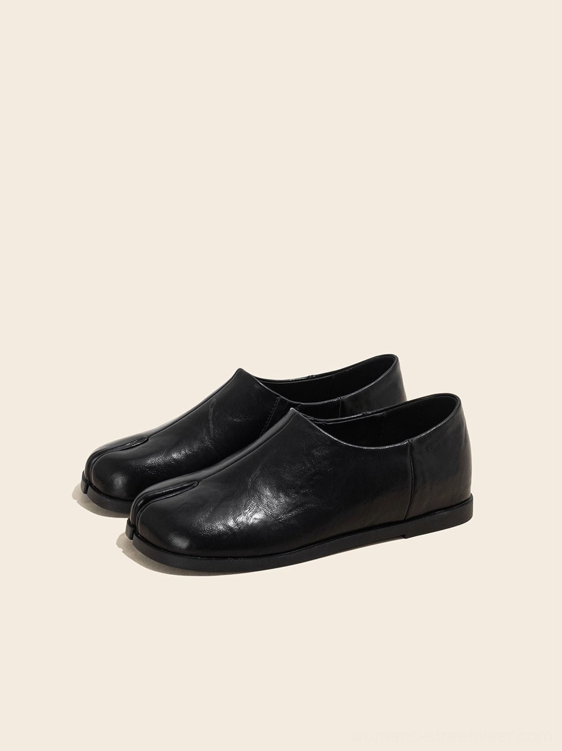 Front three-quarter view of black split-toe leather loafers showing the smooth upper, flat sole, and structured toe