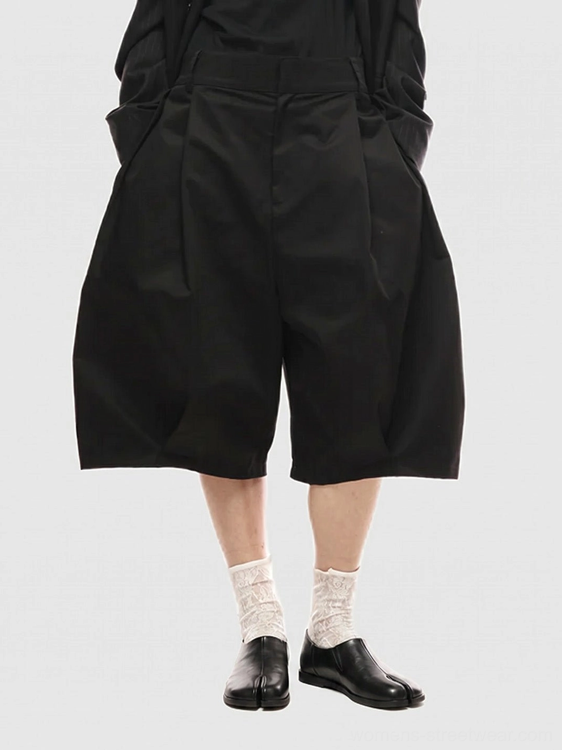 Women's black split-toe leather loafers styled with wide-leg black shorts and lace socks for minimalist streetwear