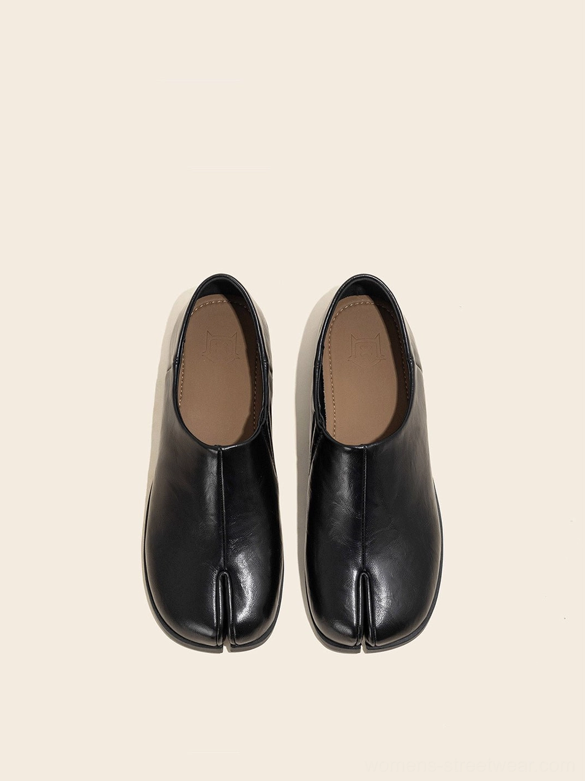 Top-down view of a pair of black split-toe slip-on loafers showing the light brown insole and minimalist toe design