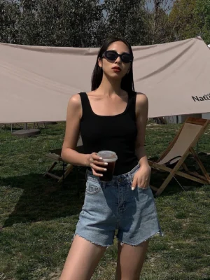 Black square neck ribbed knit camisole styled with high-waisted blue denim shorts outdoor grass setting, minimalist streetwear aesthetic front view