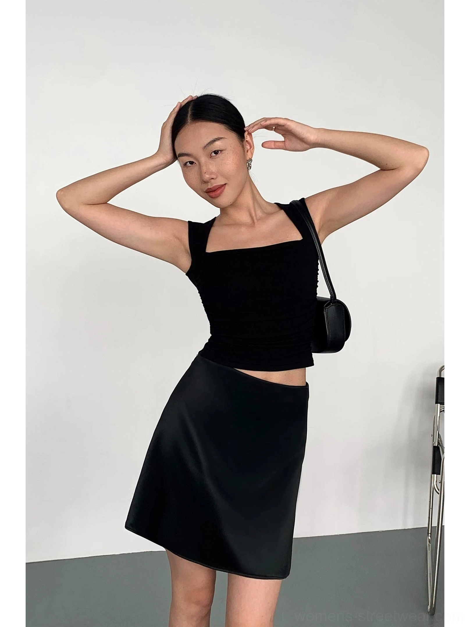 Black square neck cropped tank top shown from the side with a black mini skirt and shoulder bag