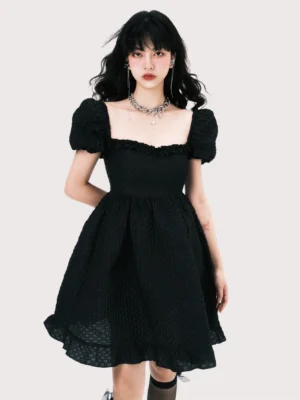 Front full-body view of a black square neck puff sleeve jacquard mini dress with ruffled neckline, empire waist, textured fabric, and A-line skirt styled with knee-high socks