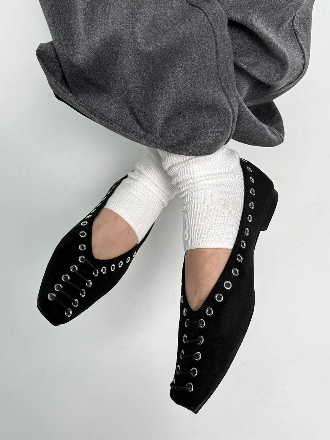 Overhead rear angle of black square-toe ballet flats showing front eyelet details with relaxed grey trousers