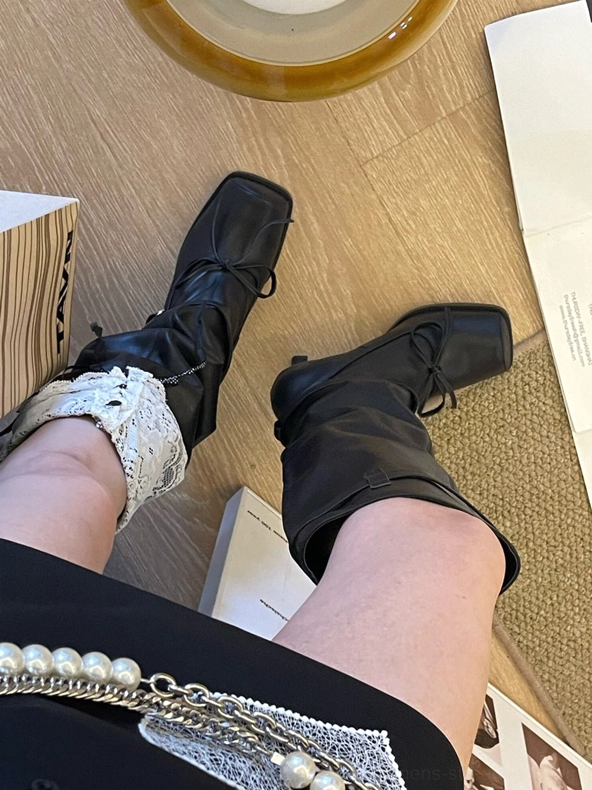 Top-down outfit view featuring black square-toe bow knee-high leather boots styled with a black skirt and white lace frill socks