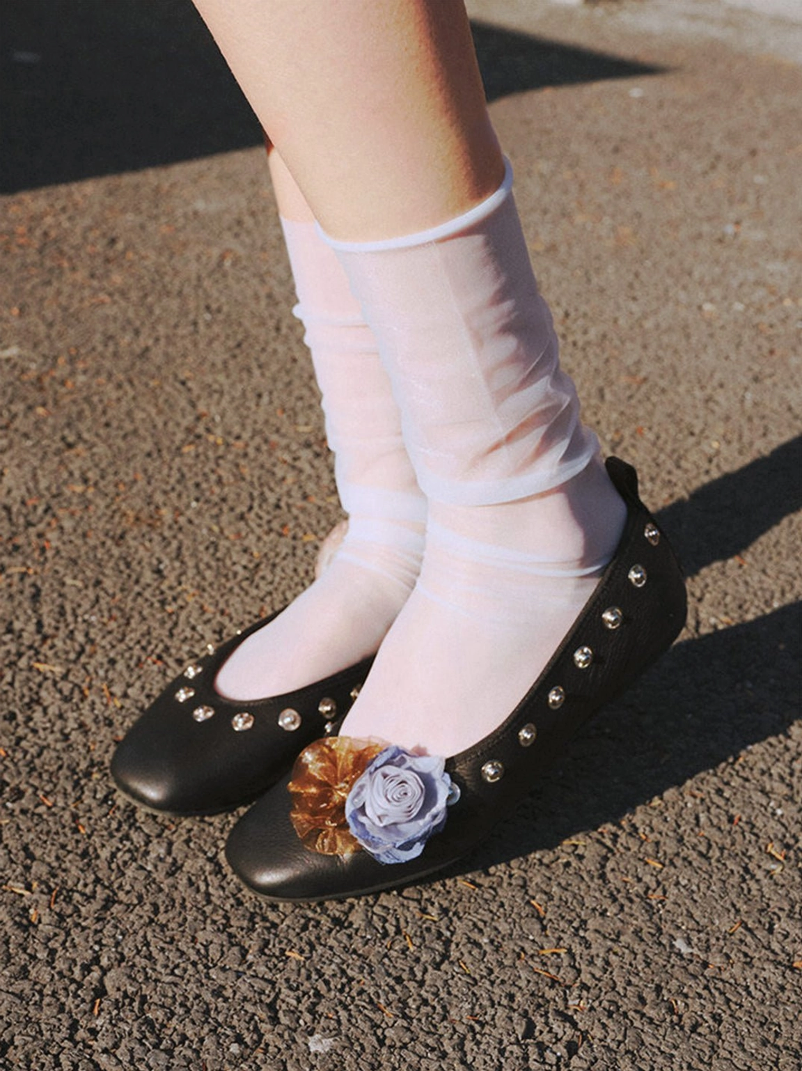 Black square-toe floral flats with studded vamp and fabric flower ornament worn outdoors