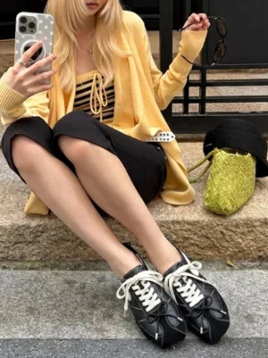Model wearing black square-toe leather sport ballet flats with white laces and cropped black pants on outdoor city stairs