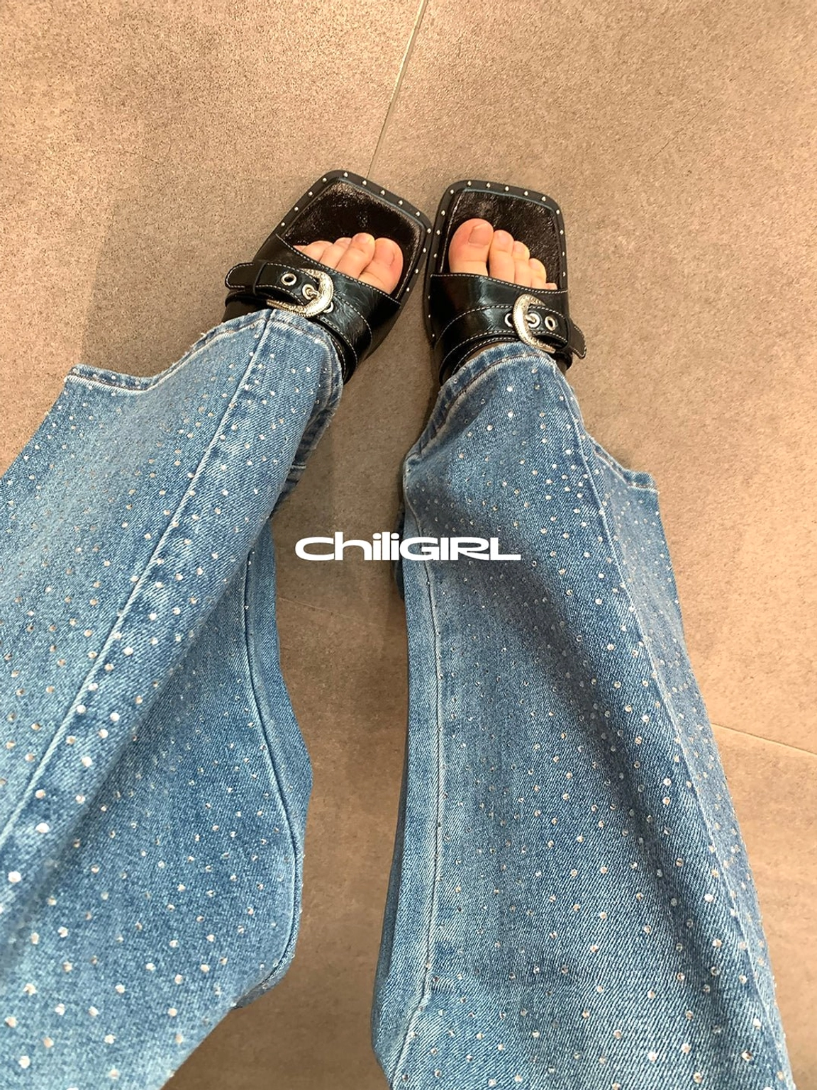 Top-down view of black square-toe buckle slide sandals styled with dotted wide-leg jeans