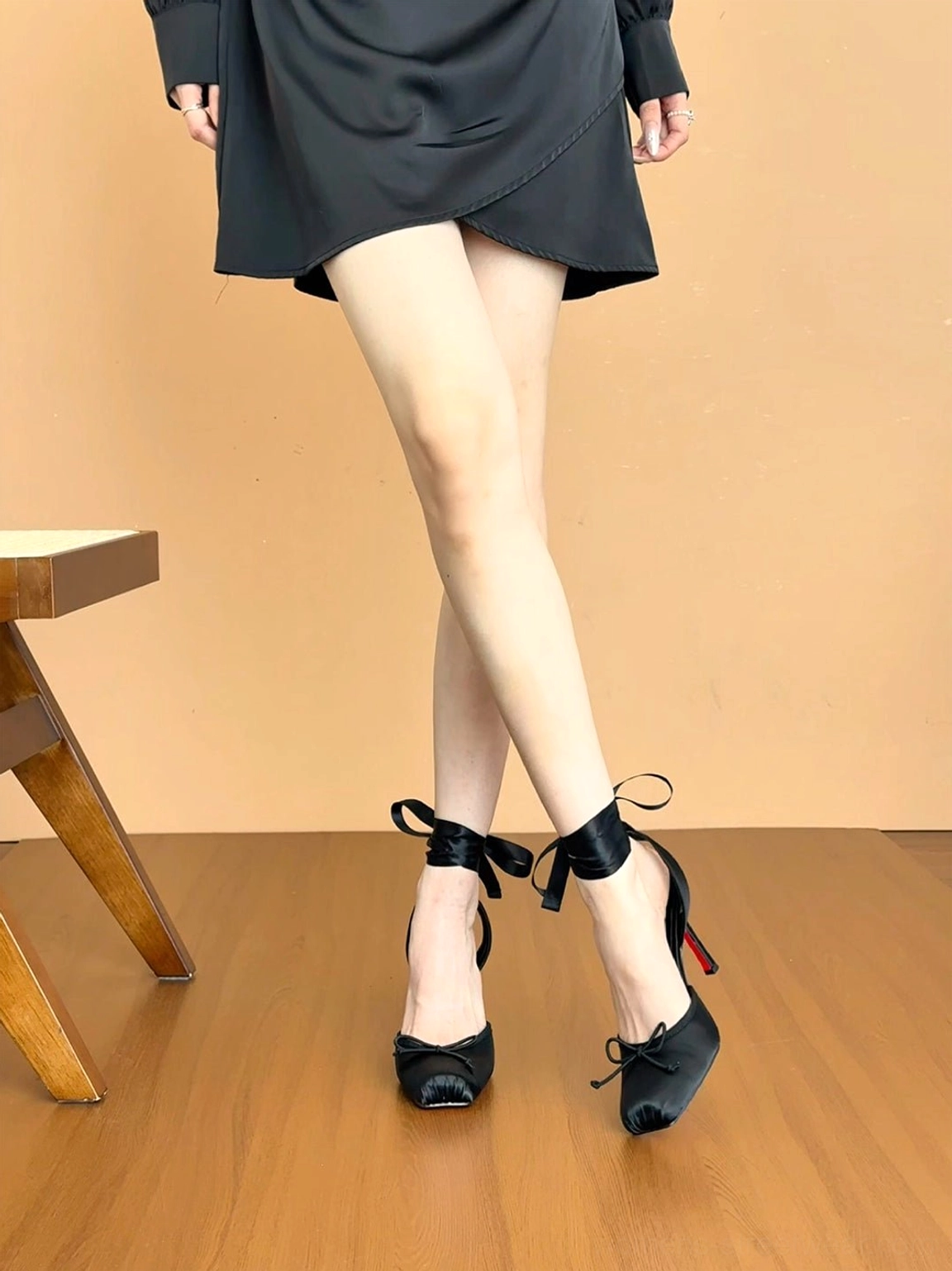 Side view of black square-toe stiletto sandals with butterfly ankle bows, high heel, and vivid red outsole