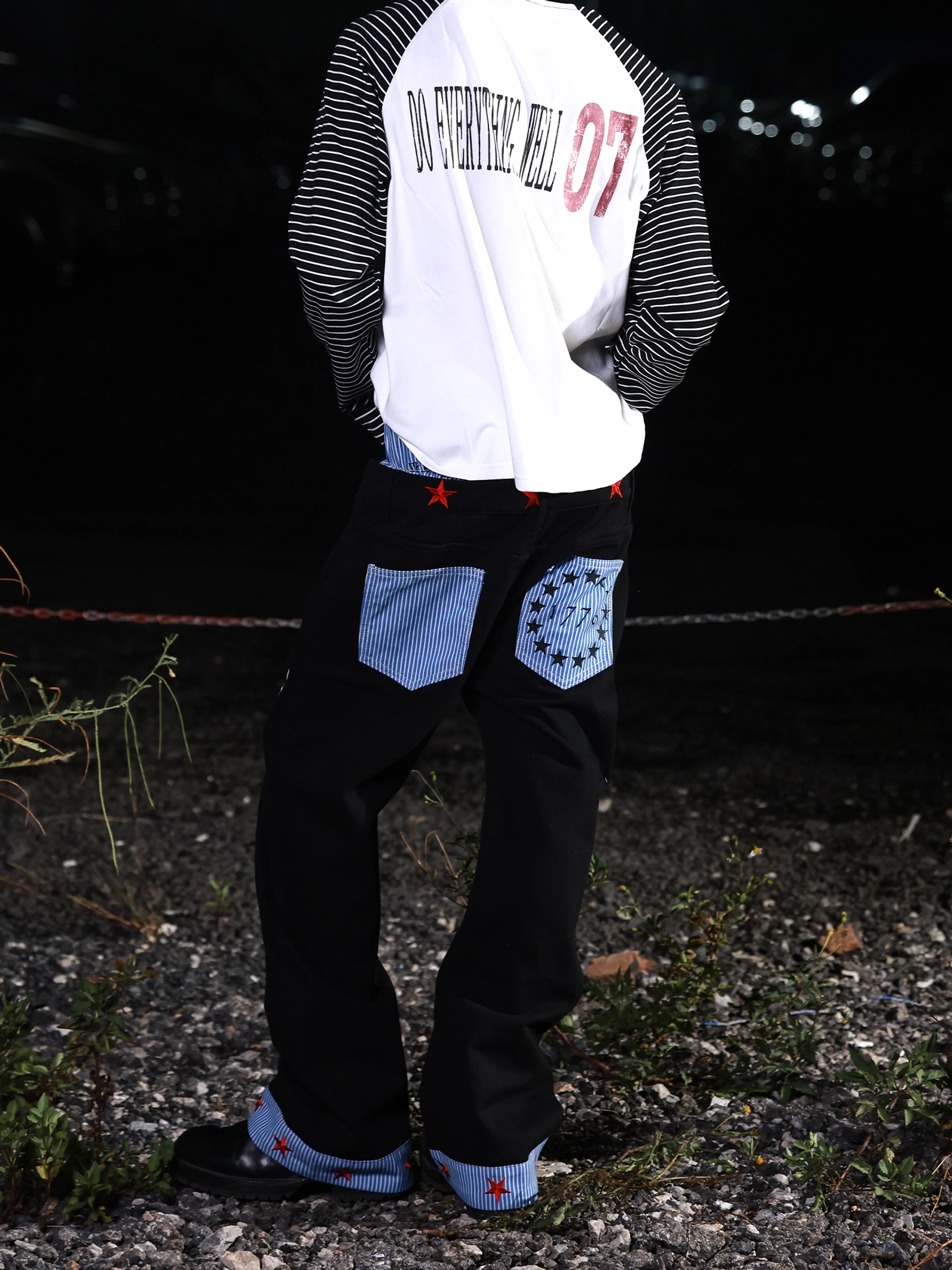Back view of black star cuff wide-leg jeans showing striped patch pockets, red star details, exposed waistband, and oversized streetwear fit
