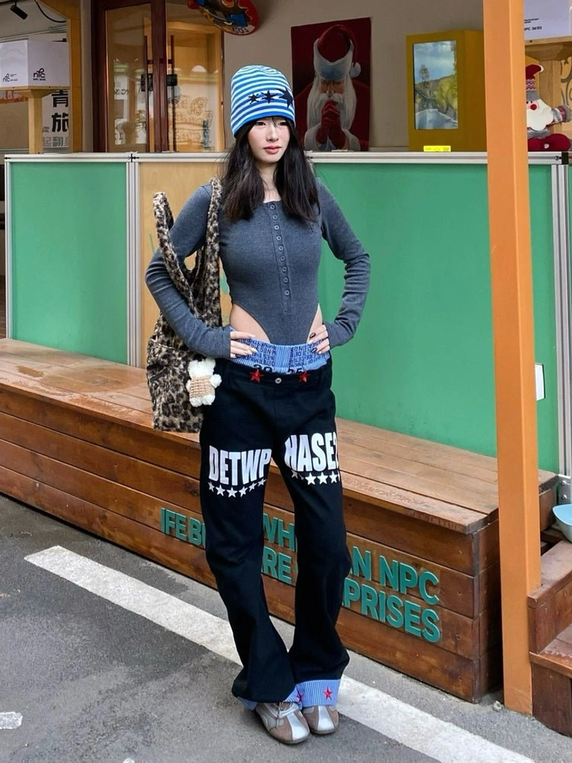Front view of black star cuff wide-leg streetwear jeans on a female model with graphic lettering, blue striped waistband, red star cuffs, and relaxed Seoul-inspired styling