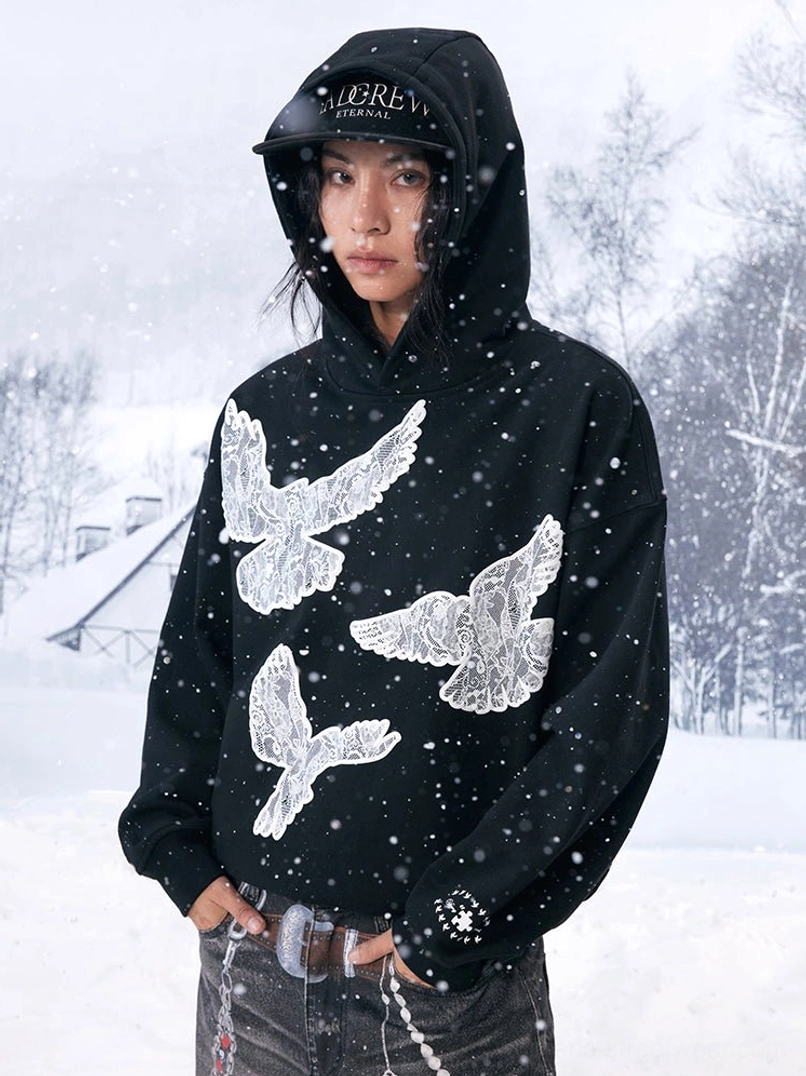 Front view of a black statement hoodie with textured dove graphics, studded accessories and chain belt styling in falling snow