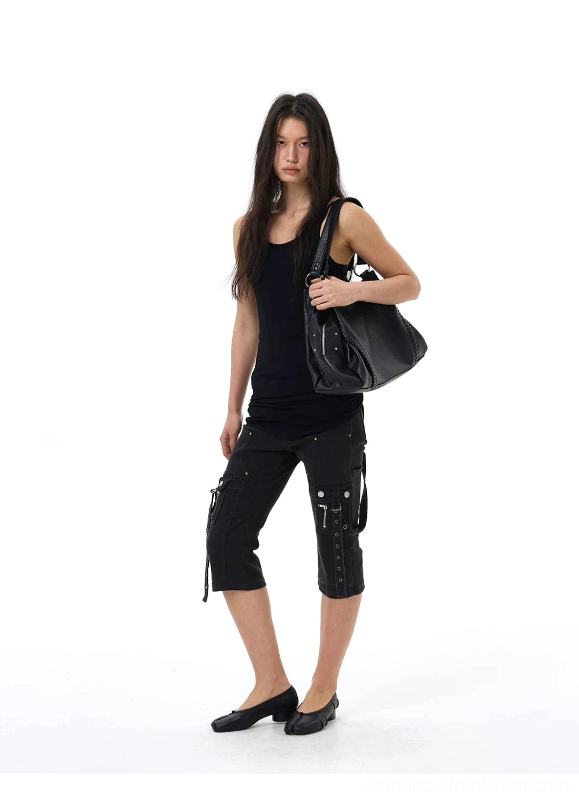 Side view of black strap cargo capri jeans styled with a black tank top, leather tote bag, and flats for a sleek urban streetwear look