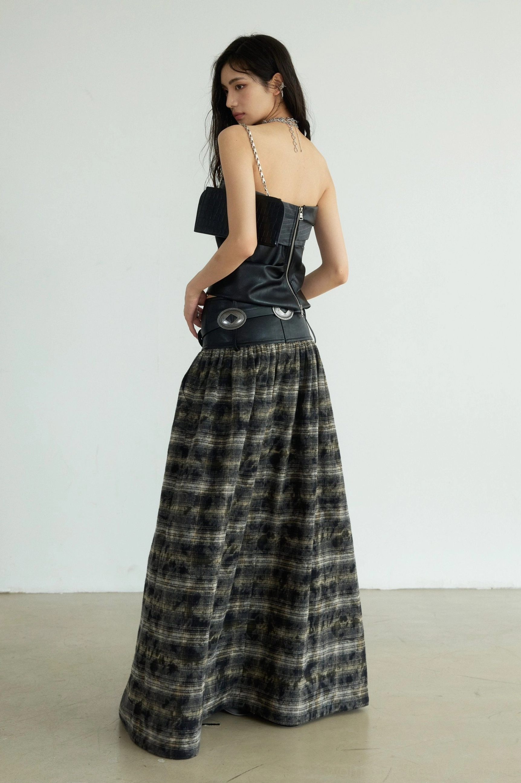 Back three-quarter view of a black strapless faux leather bustier showing its clean back design, fitted shape, and coordinated plaid floor-length skirt