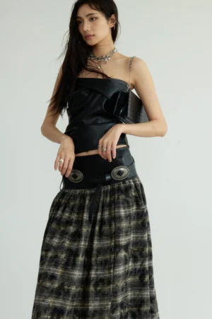 Three-quarter view of a strapless black faux leather bustier with exposed midriff, structured waistline, rounded buckle hardware, plaid skirt, and chain shoulder bag