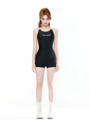 Front full-body view of a black strappy boyleg sport swim romper with lilac shoulder straps and subtle chest lettering