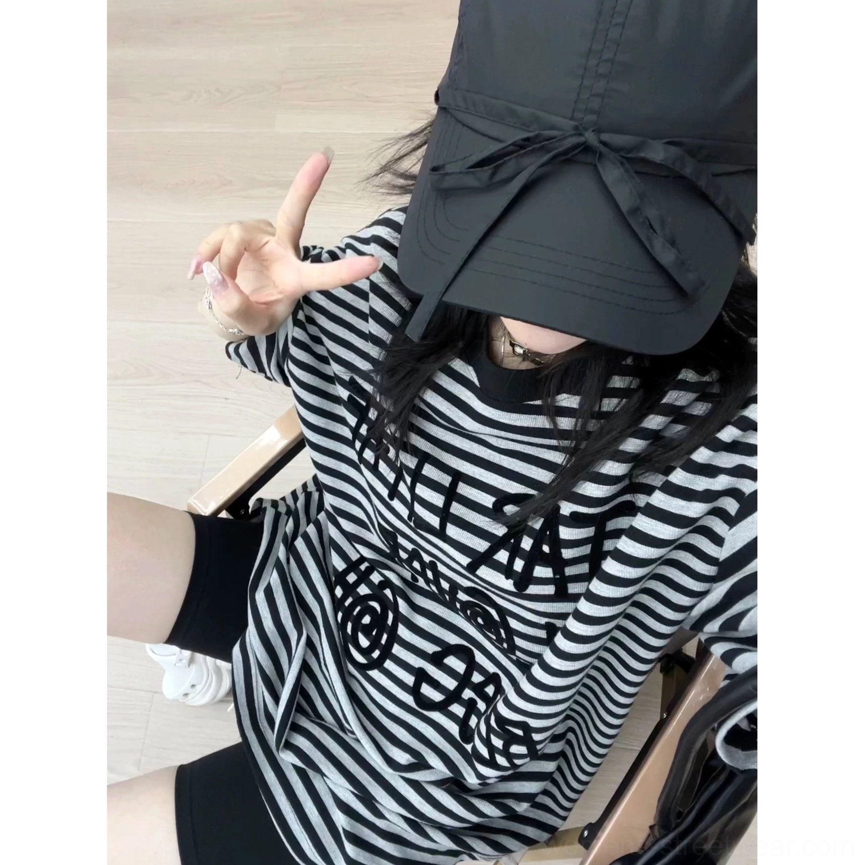 Over-the-shoulder close-up of a woman wearing a black striped oversized graphic T-shirt with chest lettering and casual Acubi-inspired styling