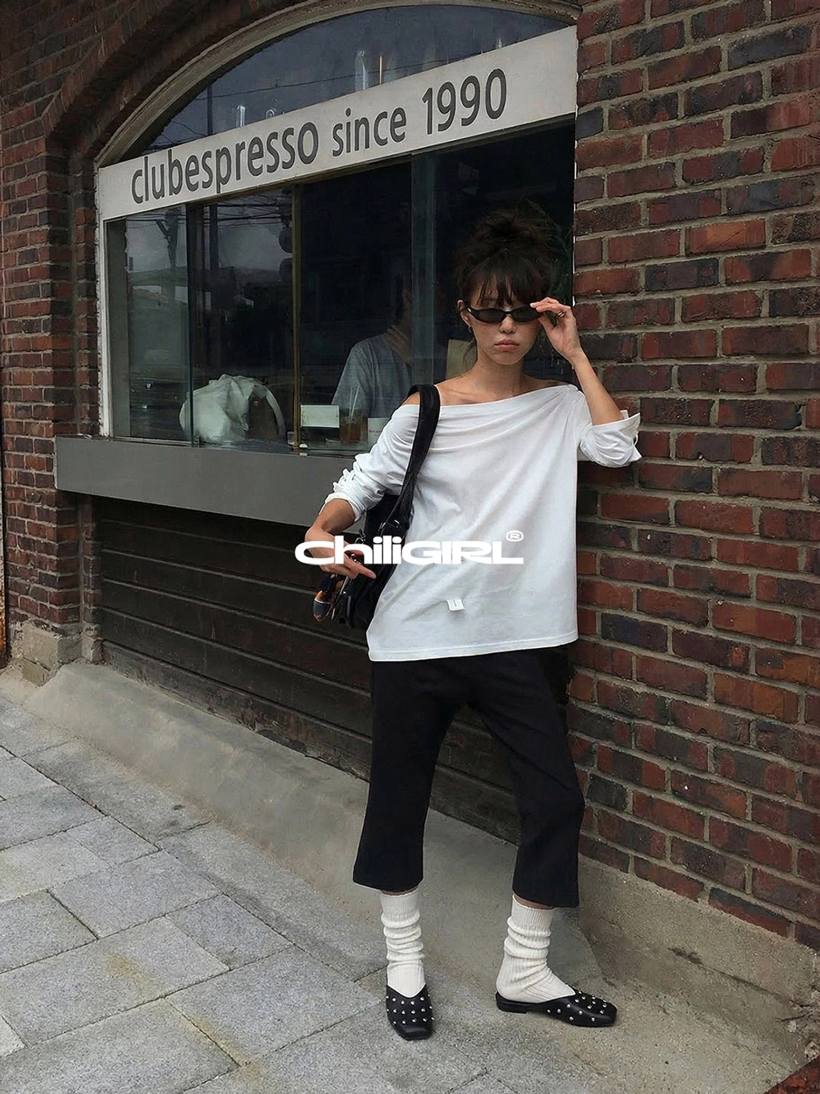 Black silver-studded mule flats styled with cropped black pants, white top, sunglasses, and a shoulder bag on a city street