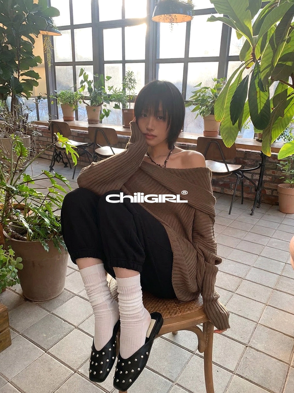 Black silver-rivet mule flats styled with slouchy white socks, cropped joggers, and a cozy brown knit top