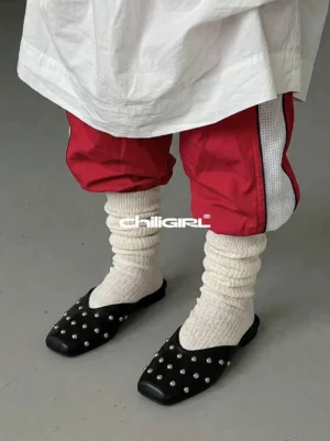 Black silver-studded mule flats styled with slouchy white socks, red-stripe track pants, and a relaxed oversized streetwear outfit