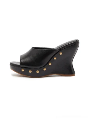 Black studded open-toe platform wedge mules shown in a side studio view with smooth wide vamp, brass-tone rivets, high sculpted wedge sole, and backless slip-on design
