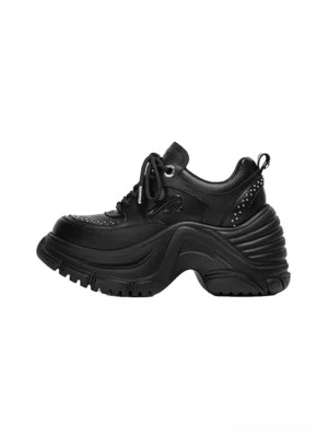 Black studded platform sneakers shown from a left three-quarter angle with a chunky sculpted rippled sole and brogue-style toe perforations