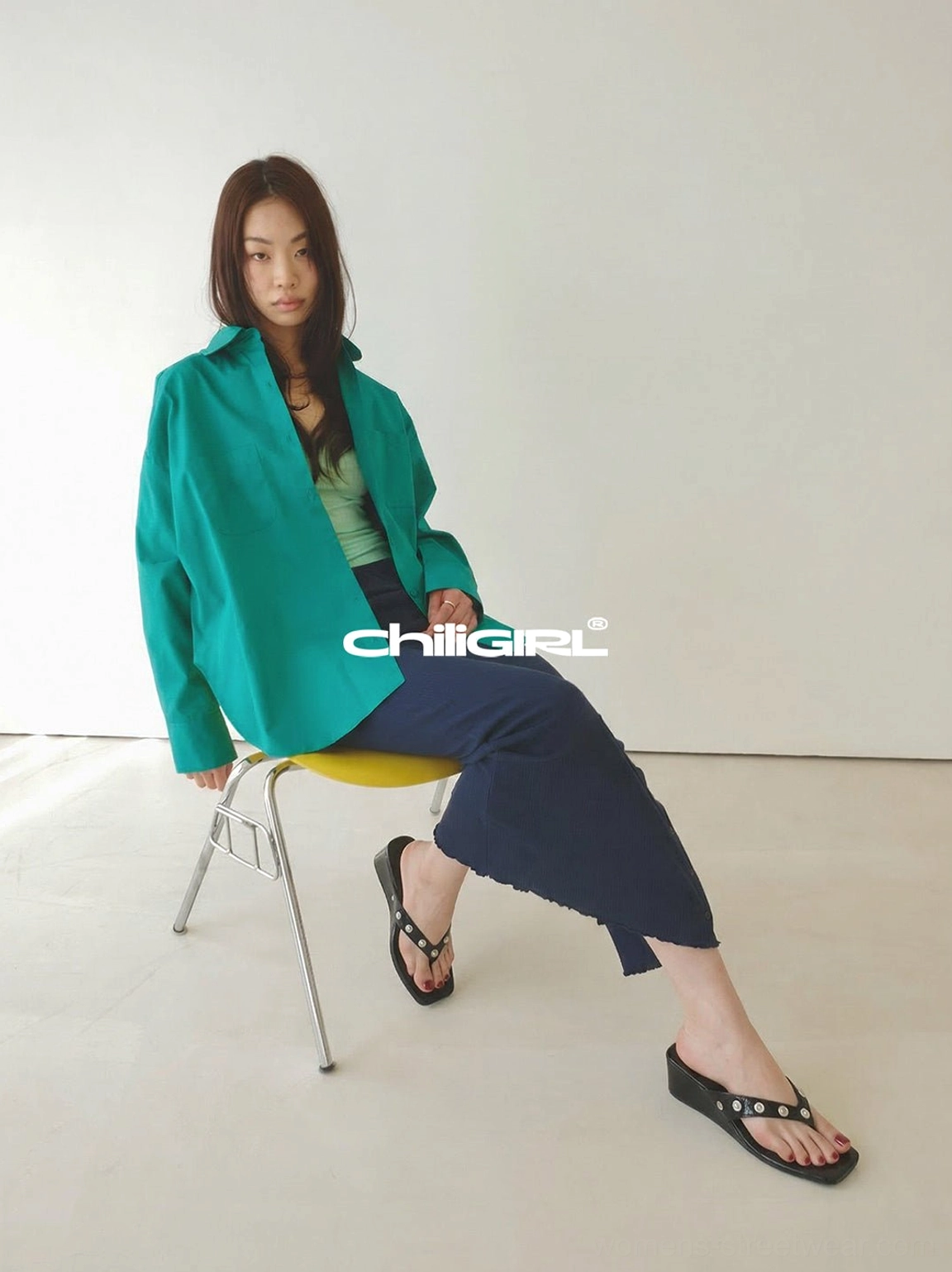 Woman seated in a green shirt and navy long skirt wearing black studded platform thong sandals in a retro casual outfit