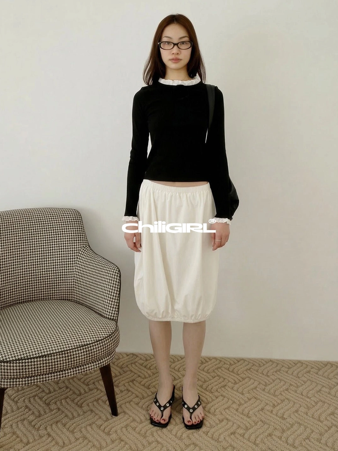 Black studded platform thong sandals styled with a black top and white midi skirt in a minimalist everyday outfit