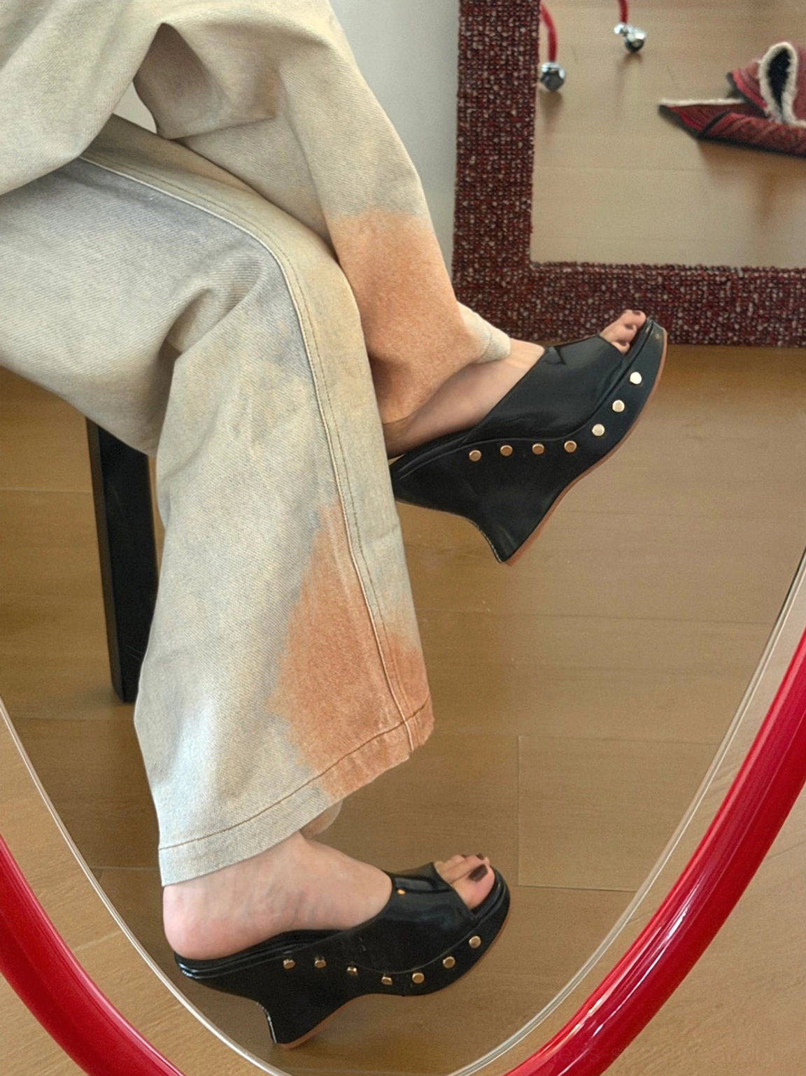 Black studded platform wedge mules worn with gradient wide-leg trousers in a mirror side view, highlighting the smooth upper and metallic rivet details