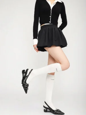 Model wearing black studded pointed-toe slingback heels with a cropped cardigan mini skirt and printed knee-high socks