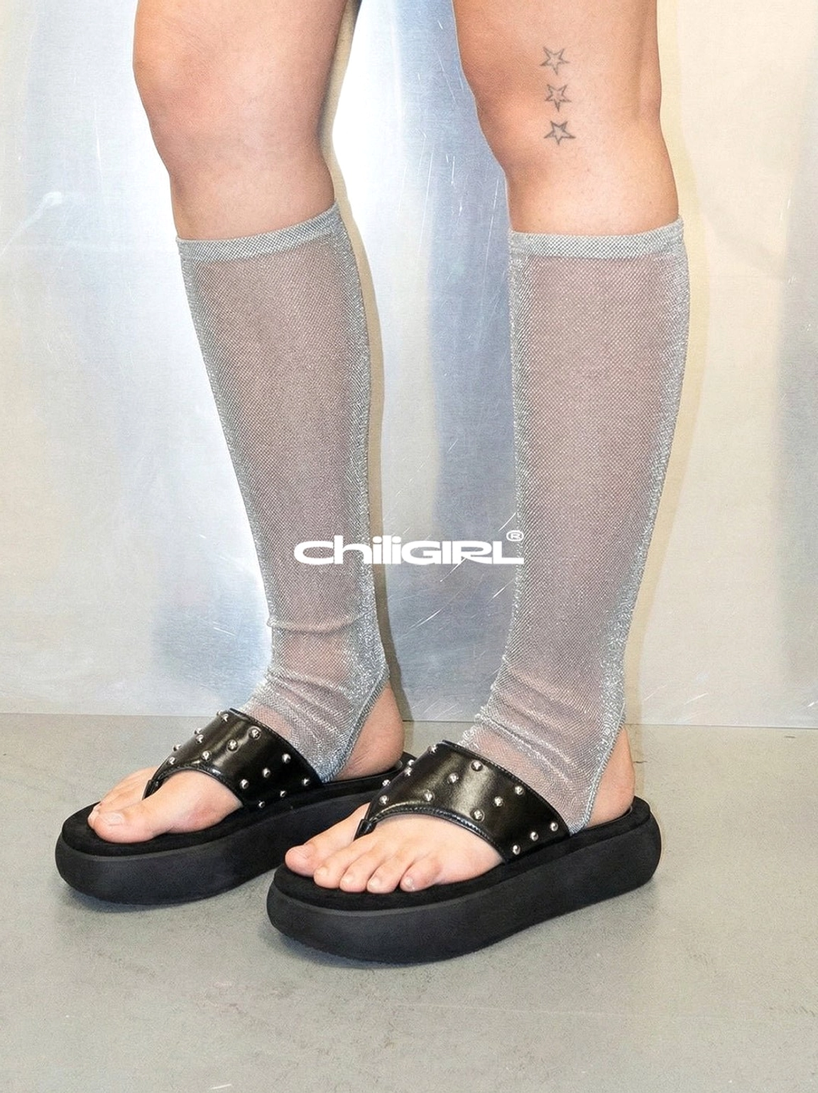Close-up of black studded thong platform sandals styled with sheer gray knee-high socks