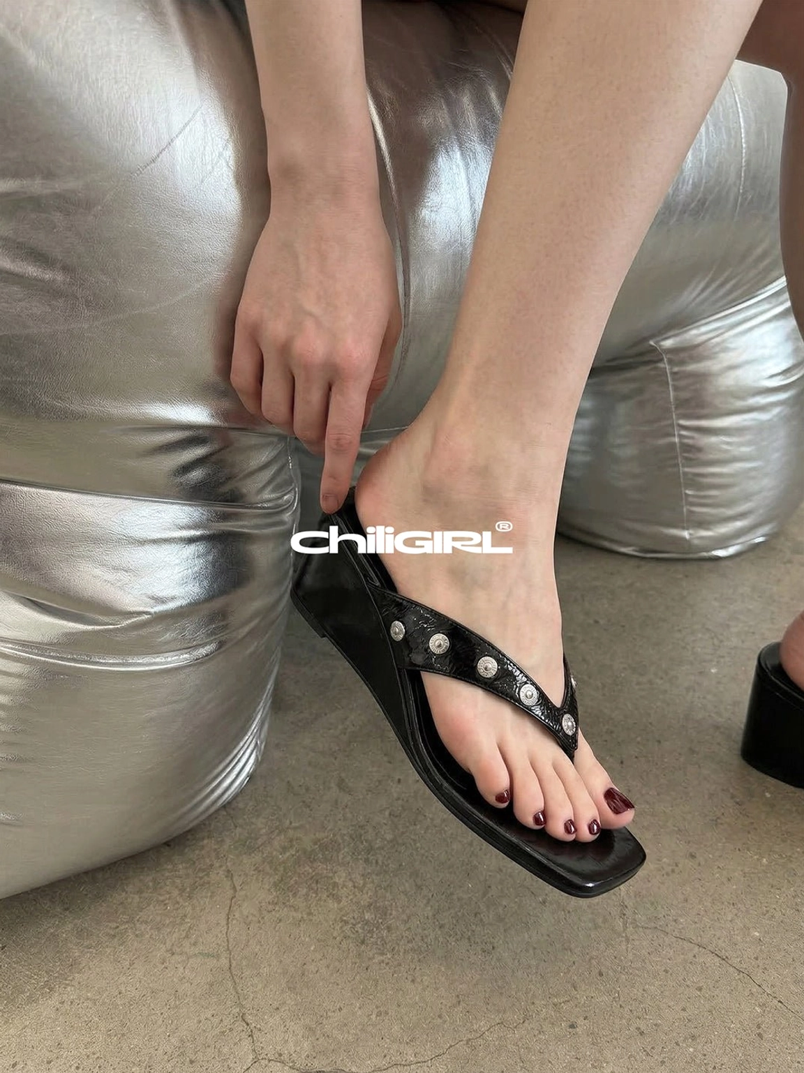 Close-up of a woman slipping on black studded thong wedge sandals with smooth PU straps and polished round silver studs