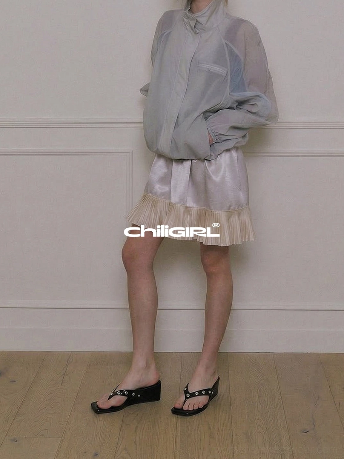 Black studded wedge heel thong sandals paired with a sheer gray coat and satin mini skirt for an elevated streetwear look