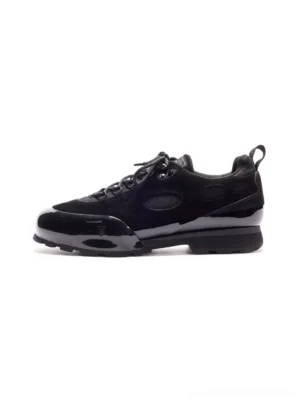 Black suede cutout chunky low-top sneakers shown in side profile with mixed suede and patent-effect panels, lace-up closure, and substantial layered rubber outsole