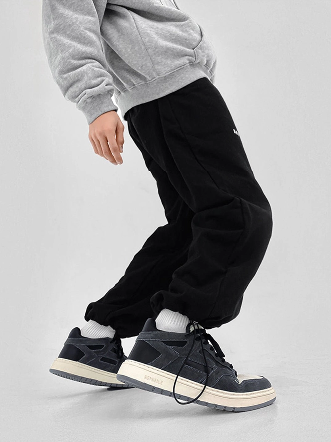 Side profile of black suede-look colorblock low-top sneakers worn with black joggers in a walking streetwear look
