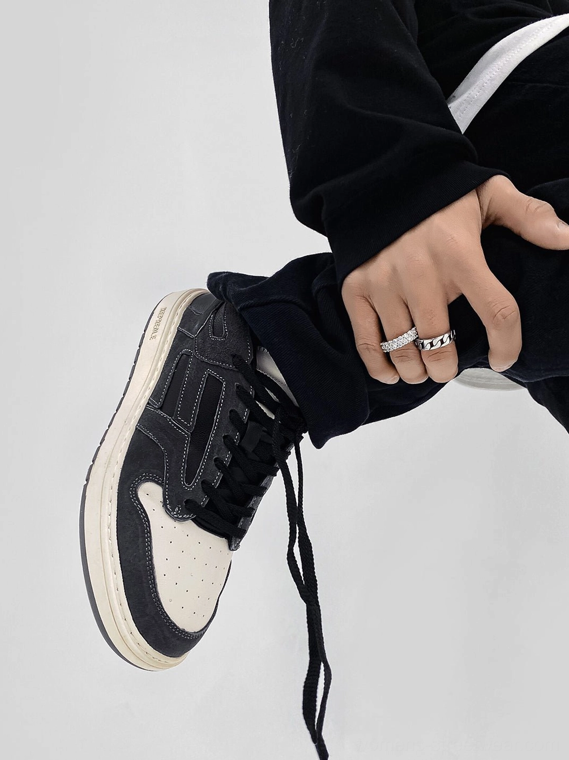 Close-up of black suede-look low-top sneaker showing off-white laces perforated toe cap and charcoal colorblock panels